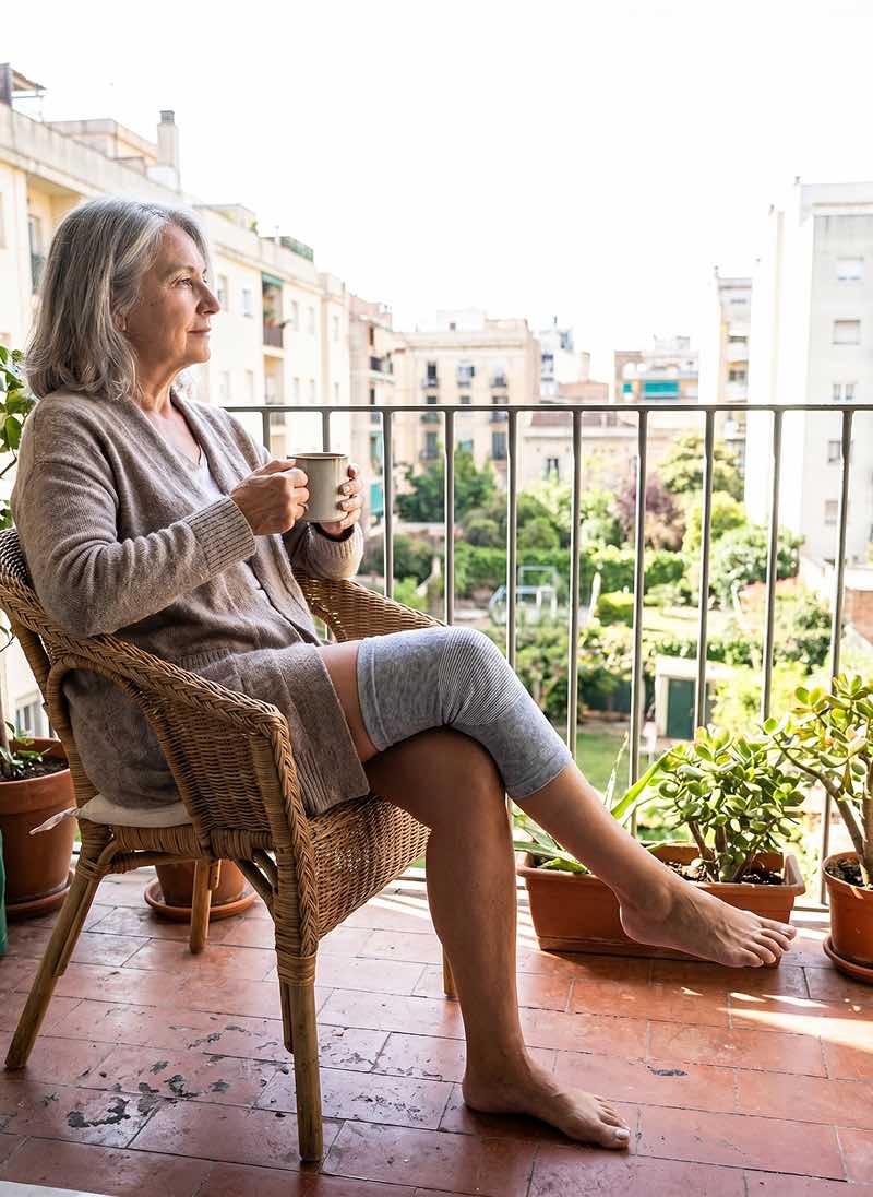 Doamnă care poartă genunchiera Presana pe balcon